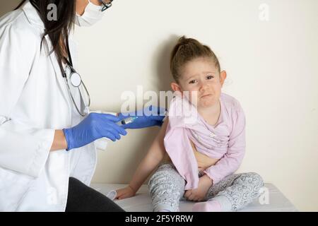 chubby bambina in esame pediatrico da parte del suo medico. vaccinato dal suo medico. Vaccino coviale selettivo per bambini Foto Stock