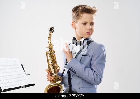 il musicista ragazzo in una classica tuta contiene un sassofono la sua mano su uno sfondo bianco Foto Stock