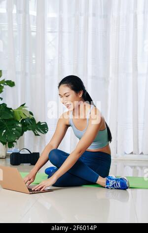 Giovane donna allegra e sottile che segue il video sullo schermo del laptop quando fare la faccia della mucca posa per la prima volta a casa Foto Stock