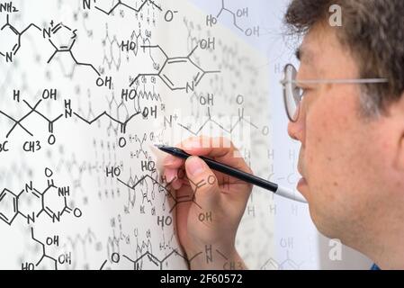 Scienziato asiatico di mezza età che scrive la formula chimica sulla lavagna bianca. Foto Stock
