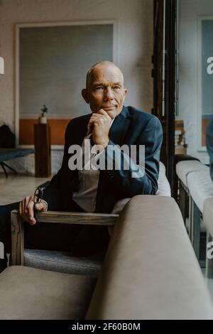 Ritratto di imprenditore maschile con la mano sul mento seduta divano in ufficio Foto Stock