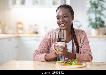 Inizio della giornata. Happy Black Woman mangiare prima colazione e bere caffè Foto Stock