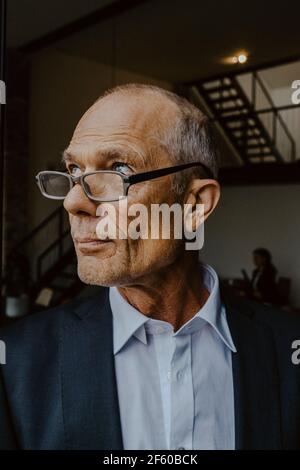 Uomo d'affari con occhiali che guardano via in ufficio Foto Stock