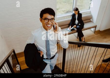 Ritratto di un uomo d'affari sorridente che parla su uno smartphone mentre si sale gradini in ufficio Foto Stock