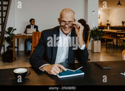 Ritratto di sorridente imprenditore maschile con gli occhi al tavolo della conferenza in spento Foto Stock
