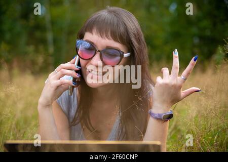 la giovane donna parla emotivamente al telefono sul prato in una giornata di sole. felice emozione sul viso Foto Stock