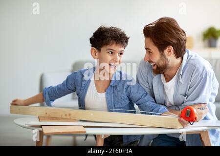 Miglior team. Allegro padre e figlio che misura la tavola di legno con nastro. Casa per la produzione di uccelli in famiglia con dettagli in legno Foto Stock