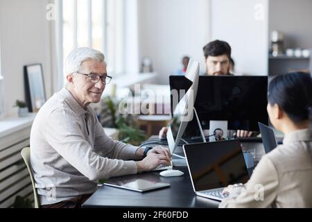 Ritratto di sorridente anziano che collabora con i giovani in ufficio moderno, concetto di cambiamento di carriera, spazio di copia Foto Stock