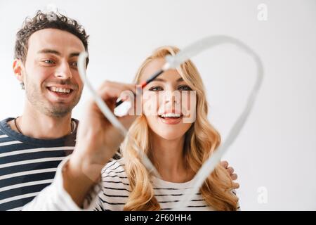 Bella giovane coppia sorridente in amore disegnando un simbolo del cuore il giorno delle valantine isolato su sfondo bianco Foto Stock