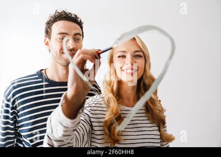 Bella giovane coppia sorridente in amore disegnando un simbolo del cuore il giorno delle valantine isolato su sfondo bianco Foto Stock