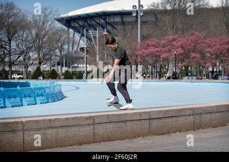 Uno skateboarder americano asiatico fa un trucco di far scorrere la sua tavola lungo un argine sottile di cemento vicino all'Unisfero nel Flushing Meadows Corona Park. Foto Stock