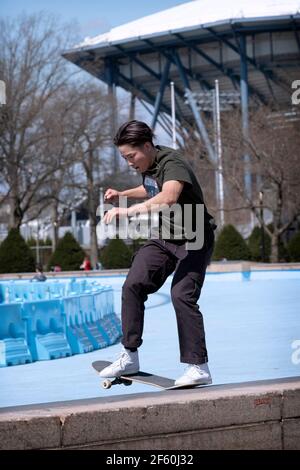 Uno skateboarder americano asiatico fa un trucco di far scorrere la sua tavola lungo un argine sottile di cemento vicino all'Unisfero nel Flushing Meadows Corona Park. Foto Stock