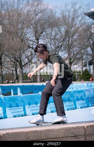 Uno skateboarder americano asiatico fa un trucco di far scorrere la sua tavola lungo un argine sottile di cemento vicino all'Unisfero nel Flushing Meadows Corona Park. Foto Stock