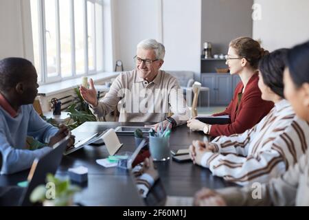 Ritratto di un uomo anziano dai capelli bianchi che istruisce un gruppo diverso di persone durante la riunione di briefing in ufficio Foto Stock