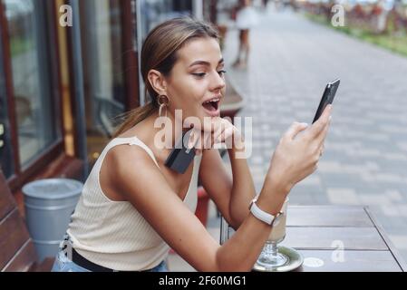 WOW! La ragazza giovane è sorpresa, guardando nello schermo del telefono e tenendo una carta di credito. La donna scioccata urla. Foto Stock