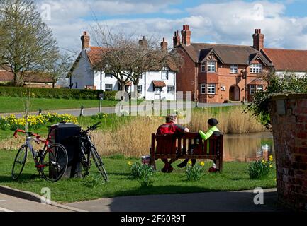 Due ciclisti maschili prendono uno sfiatatoio e mangiano i loro panini, vicino al ducklaghen nel villaggio di Askham Richard, North Yorkshire, Inghilterra Regno Unito Foto Stock