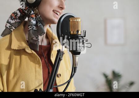 Primo piano di una donna in cuffia che canta nel microfono e registra una canzone in studio Foto Stock