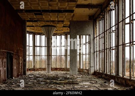 La sala in rovina di un vecchio edificio con ampie finestre. Vetro rotto sul pavimento. Foto Stock