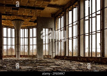 La sala in rovina di un vecchio edificio con ampie finestre. Vetro rotto sul pavimento. Foto Stock