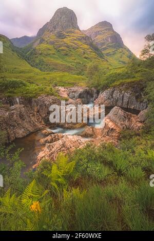 Idilliaco paesaggio montano lungo il fiume Coe fino alle tre Sorelle di Glencoe con un tramonto o un'alba colorati nelle Highlands scozzesi, Scozia. Foto Stock