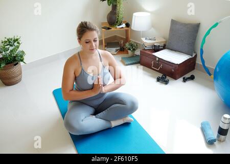 Bella giovane donna più taglia meditando su tappetino yoga con i suoi occhi chiusi Foto Stock