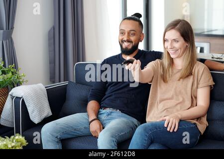 Felice giovane coppia asiatica seduta sul divano e guardando lo spettacolo in tv, relax a casa Foto Stock