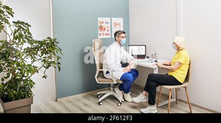 Consultazione con un esperto audiologo maschile indossando una maschera protettiva per un paziente anziano in clinica uditiva Foto Stock