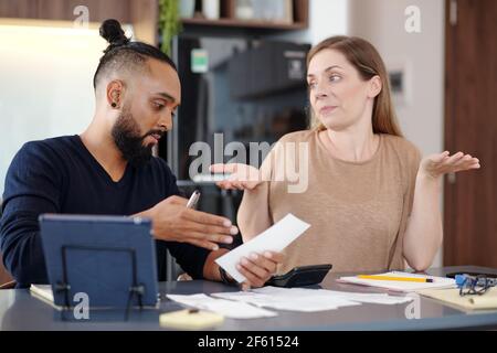 Uomo serio che mostra il disegno di legge non pagato alla moglie confusa quando sono bilancio di famiglia dicussing Foto Stock