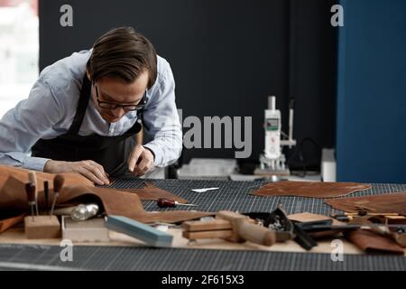 Lavoratore di fabbricazione di cuoio esperto tagliando alcuni campioni. Foto Stock