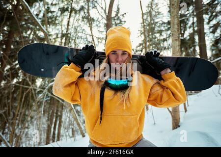 Donna snowboarder in tuta luminosa in un paio di occhiali sportivi tiene una snowboard. Sport estremi. Tempo libero Foto Stock