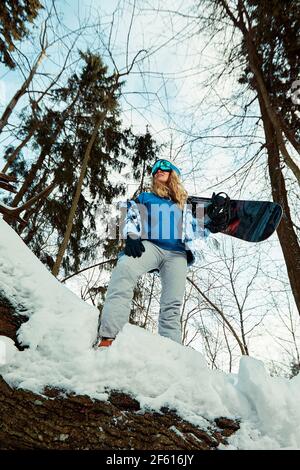 Donna snowboarder in tuta luminosa in un paio di occhiali sportivi tiene una snowboard. Sport estremi. Tempo libero Foto Stock