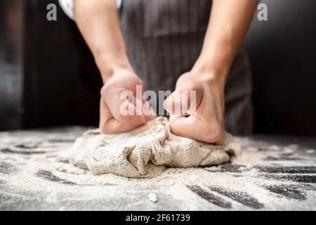 Le mani forti di un panettiere impastano l'impasto su un tavolo infarinato. Preparazione del pane. Foto Stock