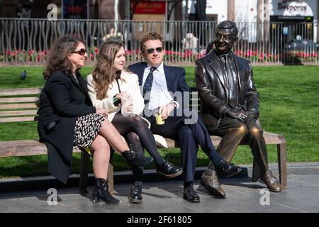 La gente si siede e chiacchiera su una panchina accanto alla statua di MR Bean a Leicester Square, Londra, Londra, dopo l'allentamento della chiusura dell'Inghilterra per consentire una maggiore libertà all'aperto. Data immagine: Lunedì 29 marzo 2021. Foto Stock