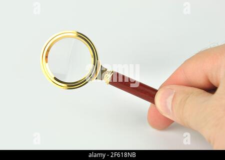 Lente d'ingrandimento in mano maschio su sfondo grigio. Analisi concettuale, ricerca, ricerca ed esame. Foto Stock