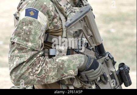 Soldato con fucile d'assalto e bandiera del Kosovo su uniforme militare. Collage. Foto Stock