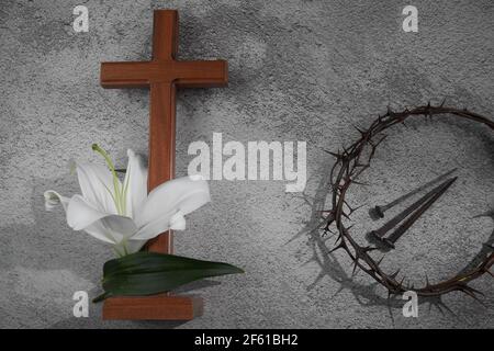 Croce con gigli bianchi e corona di spine su sfondo grigio. Concetto di Pasqua del cristianesimo. Foto Stock