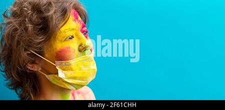 Ritratto di una donna in vernice holi di colore secco e maschera medica di protezione. Celebrazione di Holi durante una pandemia. Faccia in primo piano in colori brillanti, spac copia Foto Stock