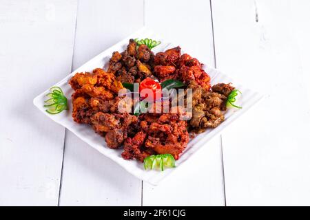 Pakoda di pollo o pakora, tre diversi sapori di pakora disposti in un piatto bianco quadrato e guarnito con pomodoro e cetriolo su uno sfondo bianco Foto Stock