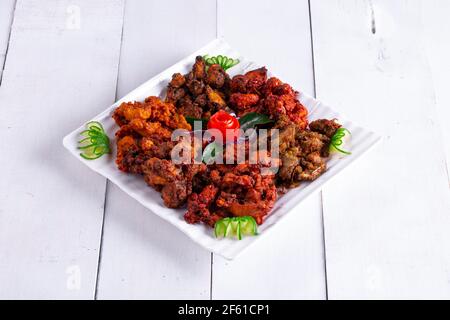 Pakoda di pollo o pakora, tre diversi sapori di pakora disposti in un piatto bianco quadrato e guarnito con pomodoro e cetriolo su uno sfondo bianco Foto Stock