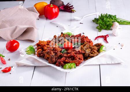 Pakoda di pollo o pakora, tre diversi sapori di pakora disposti in un piatto bianco quadrato e guarnito con pomodoro e cetriolo posto su te bianco Foto Stock