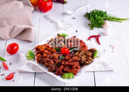 Pakoda di pollo o pakora, tre diversi sapori di pakora disposti in un piatto bianco quadrato e guarnito con pomodoro e cetriolo posto su te bianco Foto Stock