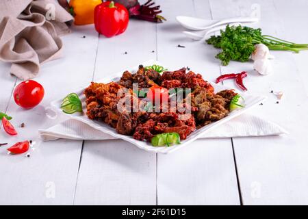 Pakoda di pollo o pakora, tre diversi sapori di pakora disposti in un piatto bianco quadrato e guarnito con pomodoro e cetriolo posto su te bianco Foto Stock