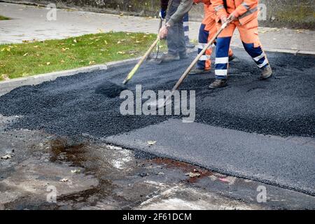 Gli addetti alla pavimentazione si spostano molto velocemente sulle pale regolando il nuovo strato di asfalto nella ricostruzione della strada. Foto Stock