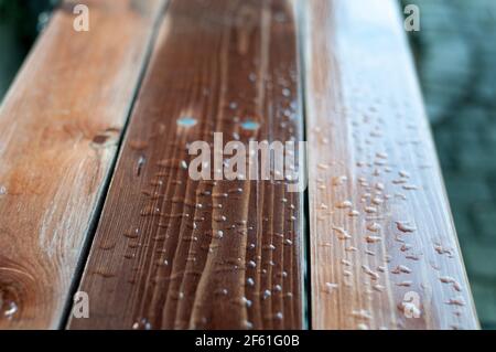 gocce d'acqua sulle tavole laccate di una panca da giardino dopo la pioggia Foto Stock