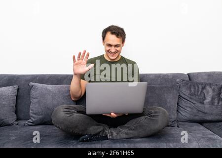 Amichevole felice giovane uomo che ondola la mano dicendo ciao guardando la macchina fotografica saluto distante amico che fa una chiamata in linea, allegro maschio vlogger registrazione Foto Stock