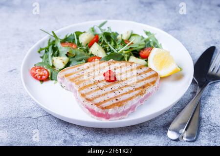 Bistecca di tonno alla griglia con verdure fresche, rucola, spinaci e limone. Primo piano. Foto Stock