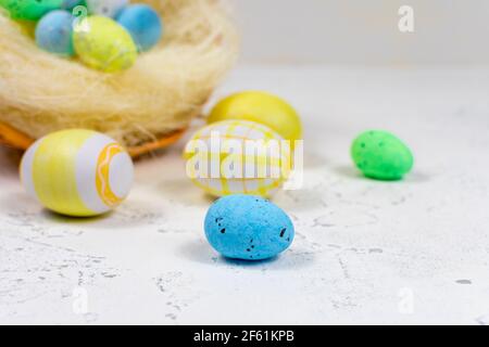 Uova di Pasqua multicolore dipinte in colori pastello su un tavolo bianco sullo sfondo di un cestino di uova di Pasqua. Messa a fuoco selettiva. Posto per un Foto Stock