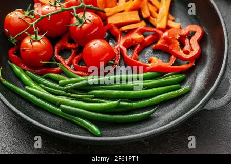 Padella con verdure gustose su sfondo scuro, primo piano Foto Stock