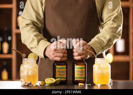 Barista con bottiglie e barattoli di birra fresca allo zenzero sul tavolo in bar Foto Stock