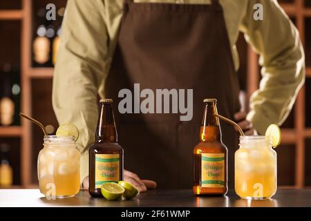 Barista con bottiglie e barattoli di birra fresca allo zenzero sul tavolo in bar Foto Stock